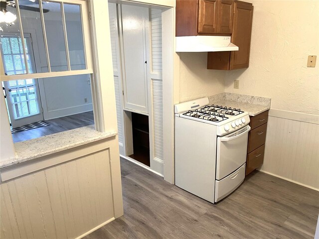 kitchen with exhaust hood, light stone counters, wood-type flooring, and gas range gas stove