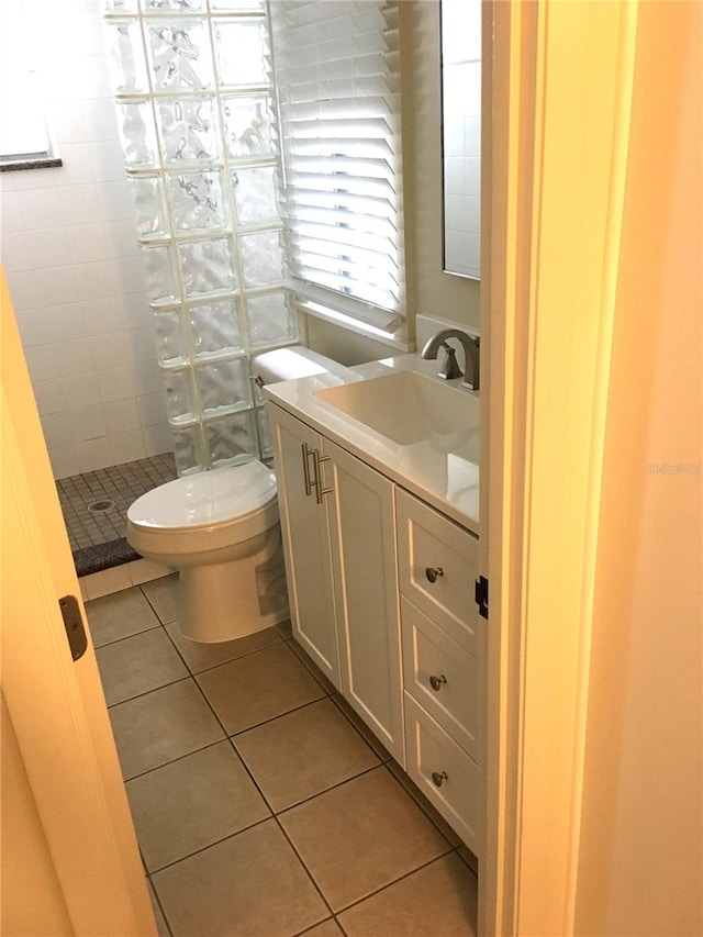 bathroom featuring vanity, a tile shower, toilet, and tile patterned floors