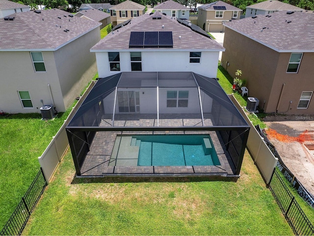 rear view of house featuring glass enclosure, a lawn, a fenced in pool, central AC, and solar panels