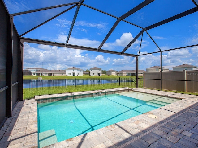 view of pool featuring glass enclosure, a water view, a yard, and a patio