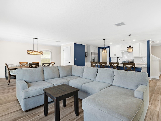 living room with light wood-type flooring, a notable chandelier, and ornamental molding