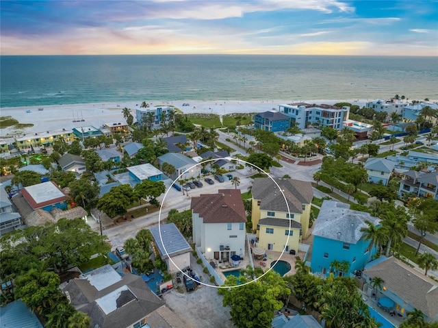 aerial view at dusk featuring a water view and a beach view