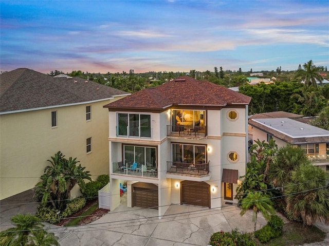 back house at dusk with a balcony and a garage