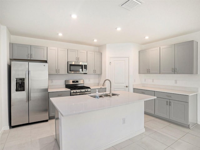 kitchen with light tile patterned flooring, an island with sink, sink, gray cabinetry, and stainless steel appliances