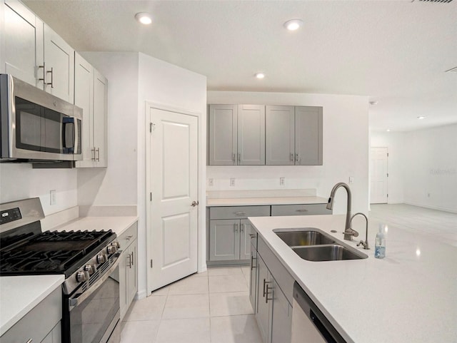 kitchen featuring a textured ceiling, light tile patterned flooring, sink, gray cabinetry, and appliances with stainless steel finishes