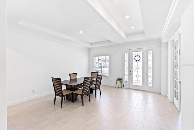 dining area featuring light wood-type flooring, a raised ceiling, and crown molding