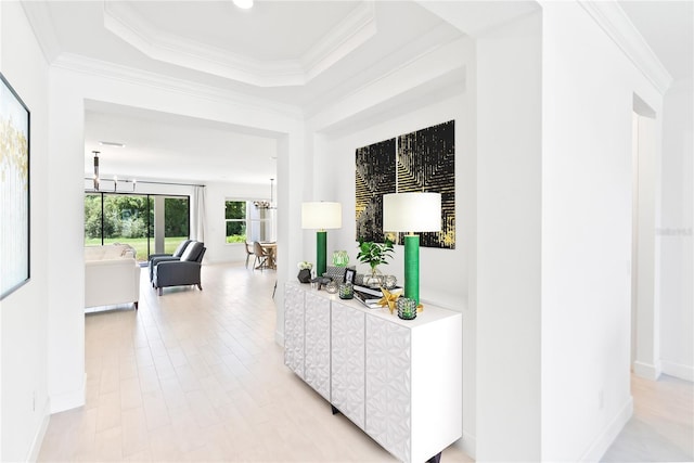 hall with light wood finished floors, baseboards, an inviting chandelier, a tray ceiling, and crown molding