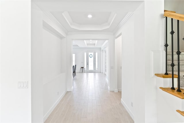 hallway featuring ornamental molding, light wood finished floors, a raised ceiling, and baseboards