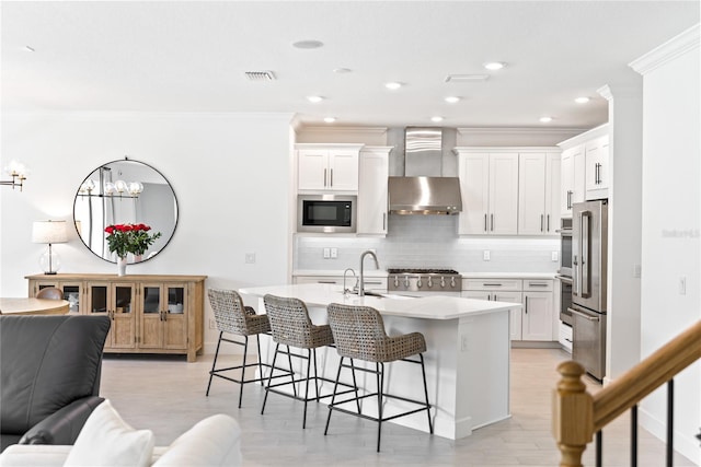 kitchen with a breakfast bar area, light countertops, a sink, built in microwave, and wall chimney exhaust hood