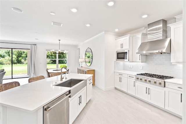 kitchen with stainless steel appliances, visible vents, backsplash, a sink, and wall chimney range hood