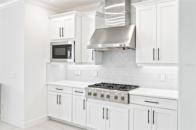 kitchen with appliances with stainless steel finishes, backsplash, ornamental molding, wall chimney exhaust hood, and white cabinets