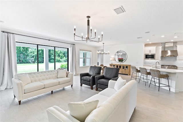 living room with light wood-style floors, recessed lighting, visible vents, and an inviting chandelier