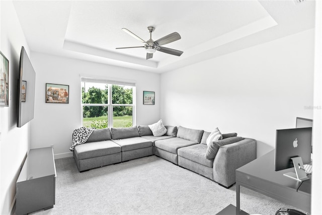 carpeted living room featuring a tray ceiling, a ceiling fan, and baseboards