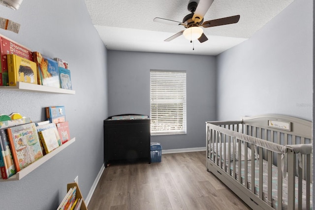 bedroom with a nursery area, ceiling fan, light hardwood / wood-style floors, and a textured ceiling