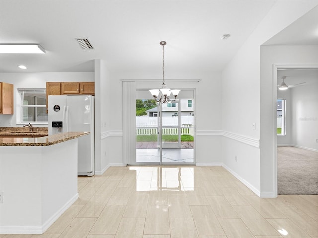 kitchen with sink, light stone counters, decorative light fixtures, light colored carpet, and white refrigerator with ice dispenser