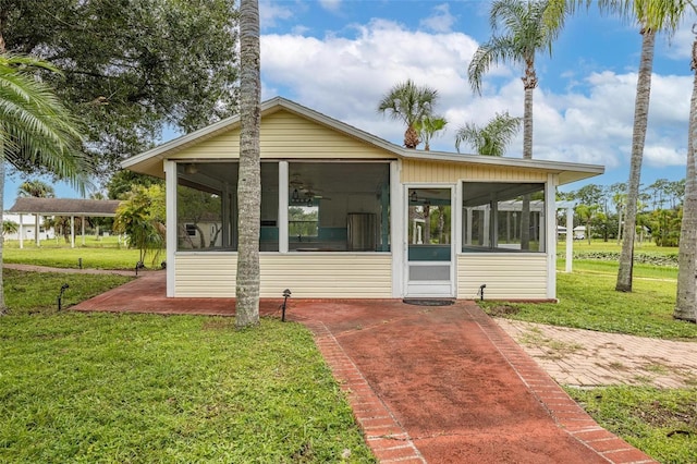 rear view of property with ceiling fan, a sunroom, and a lawn