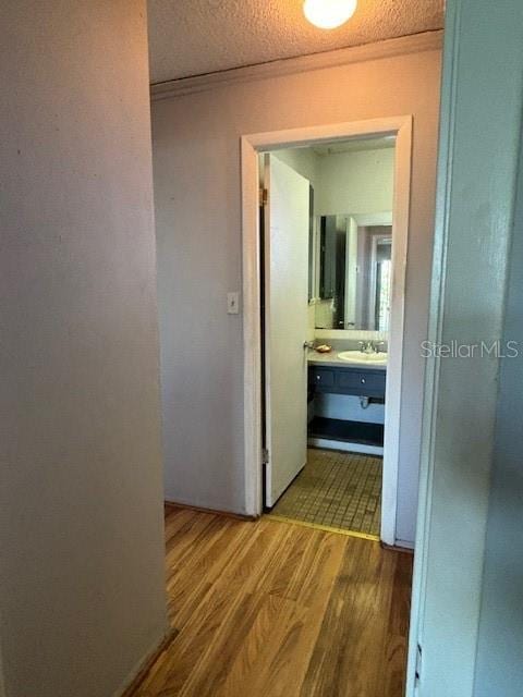 hall with sink, ornamental molding, a textured ceiling, and hardwood / wood-style flooring