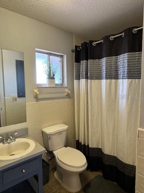 bathroom featuring toilet, vanity, tile walls, a shower with curtain, and a textured ceiling