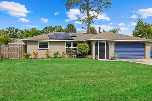 single story home featuring a garage, a front lawn, and solar panels