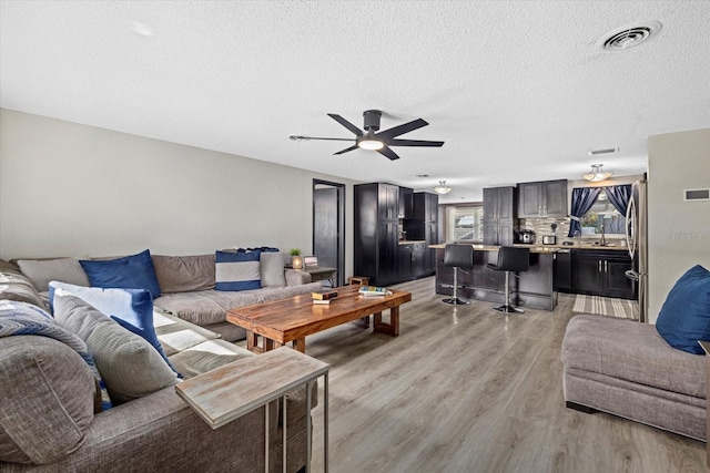 living room with light wood finished floors, ceiling fan, visible vents, and a textured ceiling