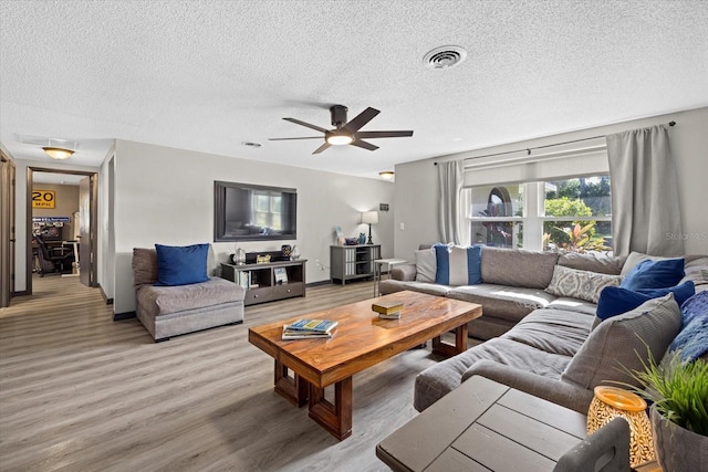 living area with baseboards, visible vents, light wood-style flooring, ceiling fan, and a textured ceiling