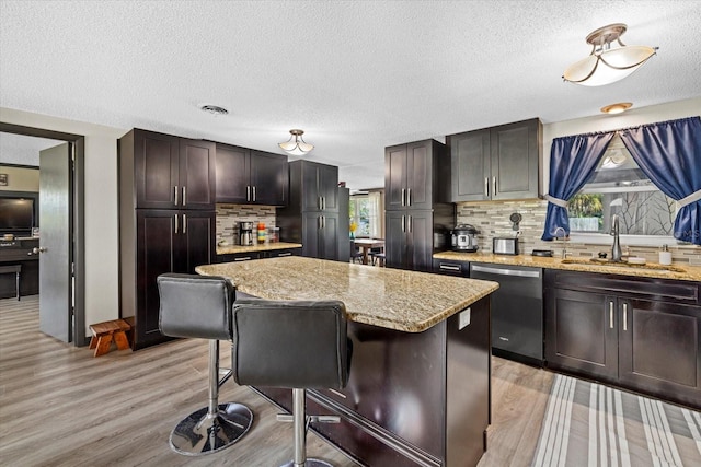 kitchen with visible vents, dishwasher, a kitchen island, a kitchen breakfast bar, and a sink