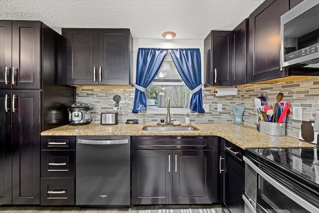 kitchen featuring appliances with stainless steel finishes, backsplash, a sink, and light stone countertops