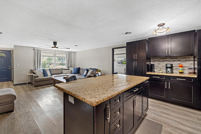 kitchen featuring open floor plan, light wood finished floors, visible vents, and tasteful backsplash