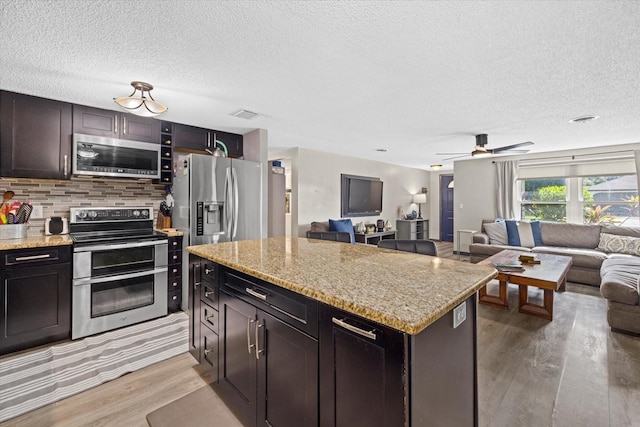 kitchen with light wood-style flooring, stainless steel appliances, open floor plan, backsplash, and a center island