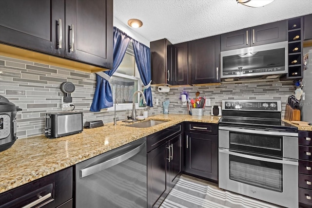 kitchen featuring tasteful backsplash, light stone counters, stainless steel appliances, a textured ceiling, and a sink