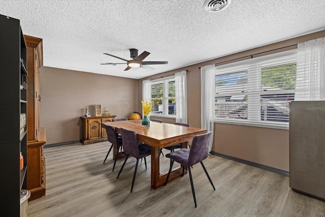 dining area with light wood-style flooring, visible vents, ceiling fan, and a textured ceiling