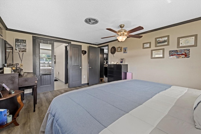 bedroom featuring ornamental molding, visible vents, a textured ceiling, and wood finished floors