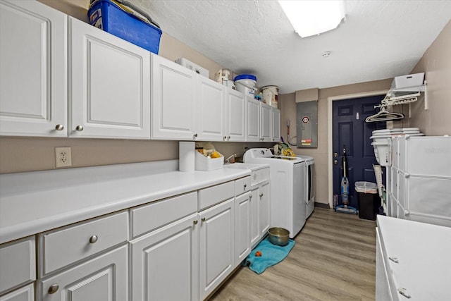 clothes washing area with washer and clothes dryer, cabinet space, a textured ceiling, light wood-type flooring, and electric panel