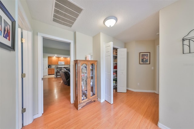 hallway with light hardwood / wood-style flooring and a textured ceiling