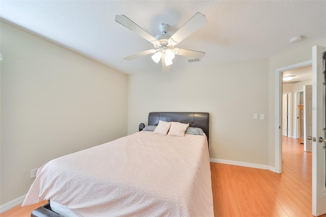 bedroom with ceiling fan, light hardwood / wood-style floors, and a textured ceiling