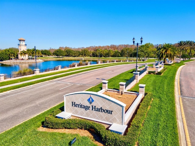 community / neighborhood sign featuring a water view and a lawn