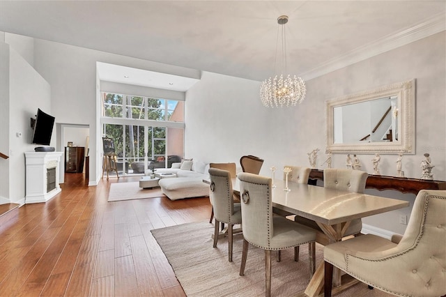 dining area with hardwood / wood-style flooring, ornamental molding, a fireplace, and a notable chandelier