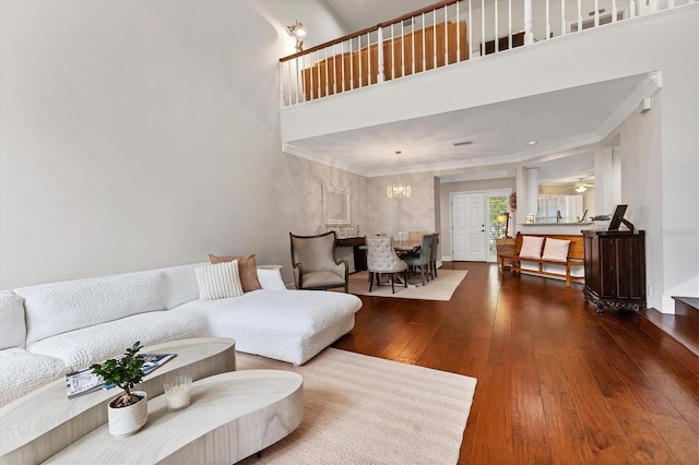 living room featuring dark wood-type flooring, crown molding, ceiling fan with notable chandelier, and a high ceiling