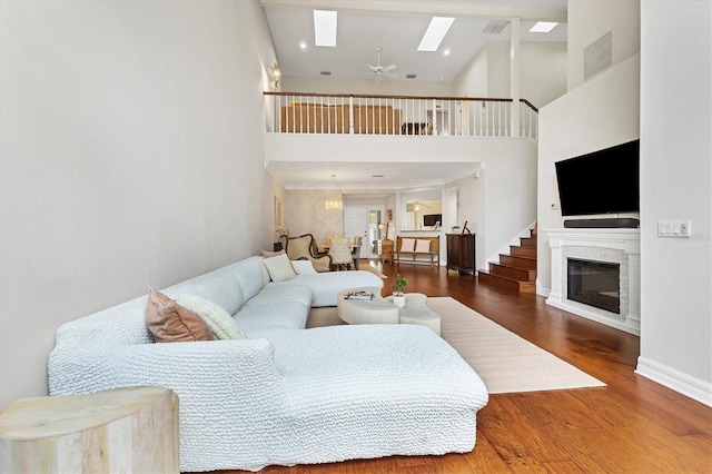 living room featuring a skylight, wood-type flooring, ceiling fan, and a high ceiling