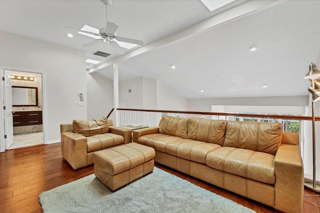 living room with ceiling fan, wood-type flooring, and vaulted ceiling with skylight