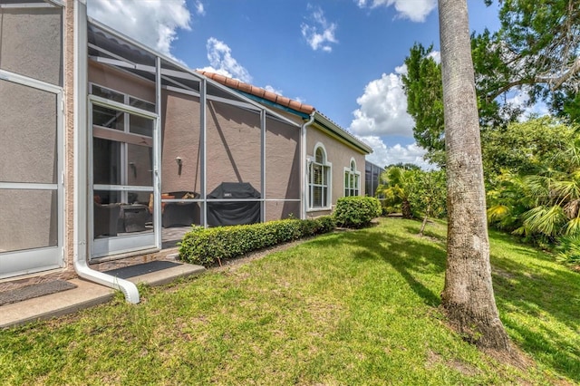 view of side of property featuring a lawn and glass enclosure