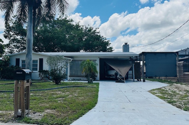 view of front facade with concrete driveway, a chimney, an attached carport, a front lawn, and stucco siding