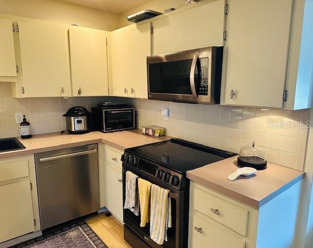 kitchen with stainless steel appliances, light countertops, a sink, and backsplash