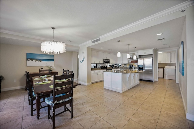 kitchen with appliances with stainless steel finishes, washer / dryer, white cabinets, hanging light fixtures, and a kitchen island with sink