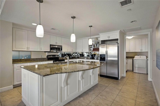 kitchen with appliances with stainless steel finishes, a center island with sink, light tile patterned floors, washer / dryer, and white cabinetry