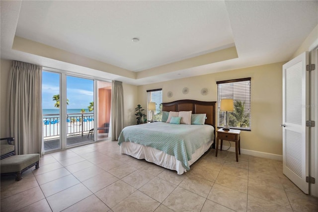 tiled bedroom with a raised ceiling, multiple windows, access to exterior, and a water view