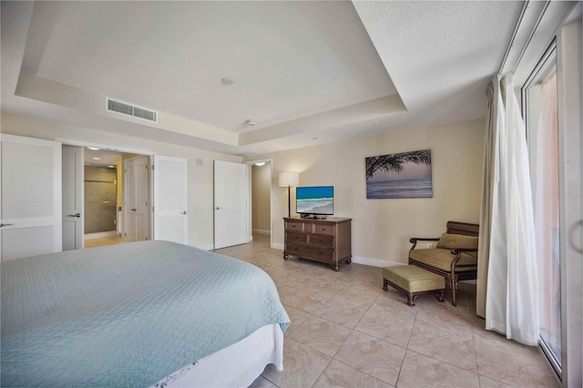 tiled bedroom with a tray ceiling and connected bathroom