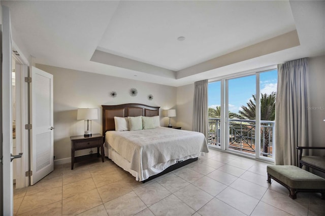 bedroom with light tile patterned floors, access to exterior, and a tray ceiling