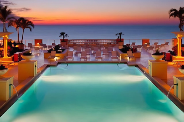 pool at dusk with a water view and a patio area