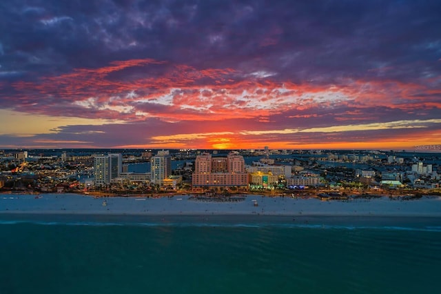 aerial view at dusk featuring a water view and a view of the beach